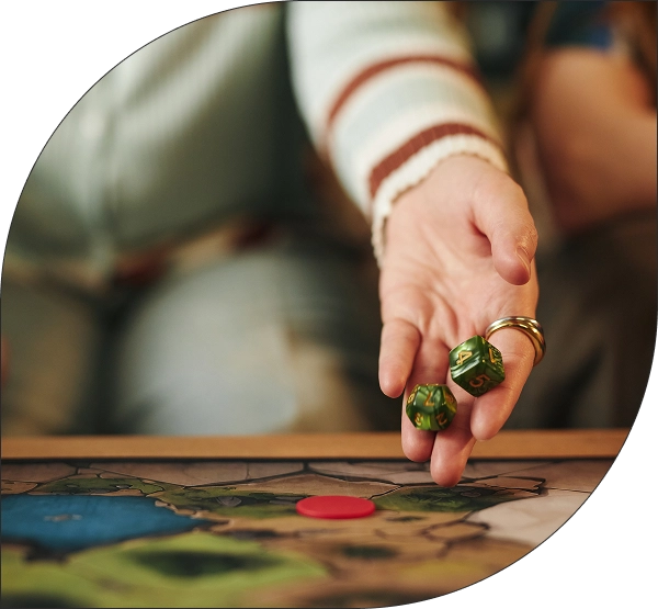 Een speler gooit groene veelvlakkige dobbelstenen op de kaart van een fantasy-avonturenbordspel tijdens een spannende sessie van een rollenspel.